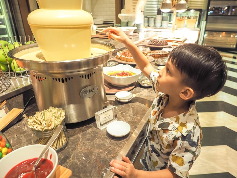 A boy dipping a treat into a chocolate fountain in a five star hotel buffet at Grand Hyatt taipei