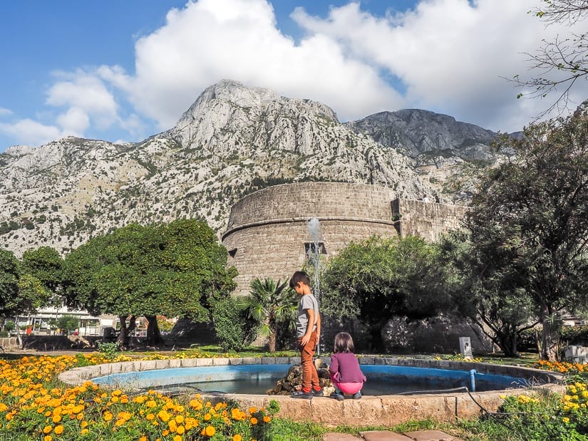 Our kids in a park by a water fountain in front of Kampana Tower and Citadel, Kotor Old Town