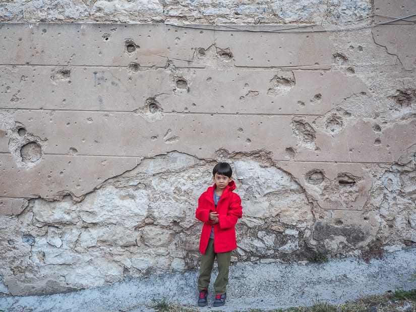 My son in front of a wall damaged by gunshots in Mostar