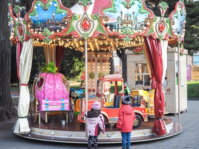 Our kids beside a merry-go-round (carousel) at Karlsplatz Christmas Market, perhaps the most family-friendly Christmas market in Vienna