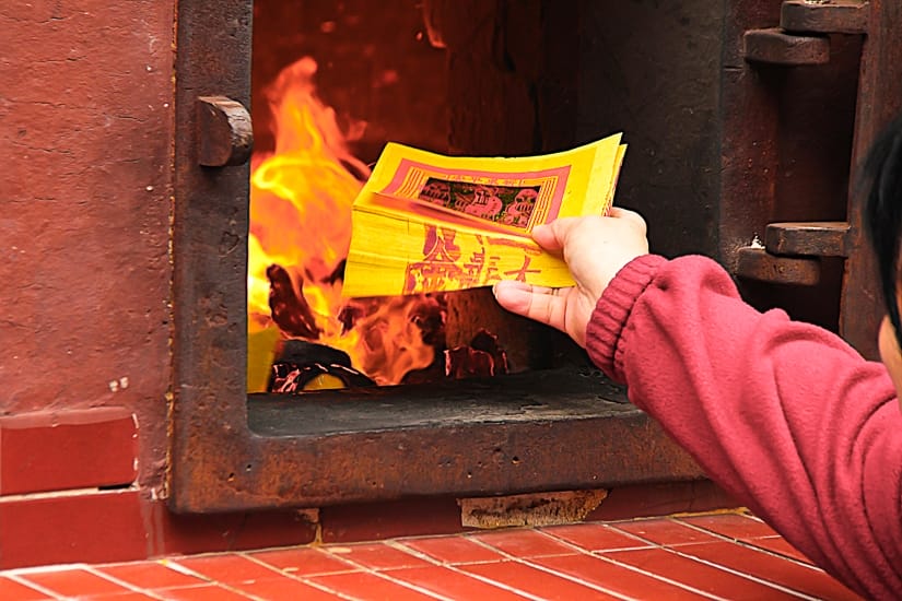 A hand putting some ghost money into a fire, part of the rituals that take place during Ghost Month in August in Taipei