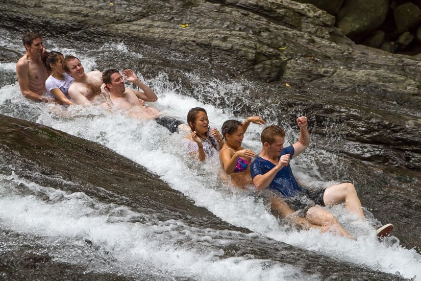 A group of people sliding down a rock slide on Jiajiuliao Stream river tracing run, Wulai
