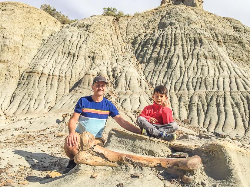 Me and my son sitting beside a dinosaur bone half buried in the ground