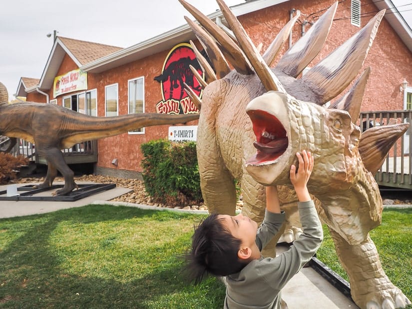 Kid looking a dinosaur statue in front of Jurassic Store DIno World, Drumheller