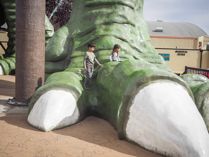 Two kids climbing on the feet of the World's Largest Dinosaur, the giant T-Rex in Drumheller