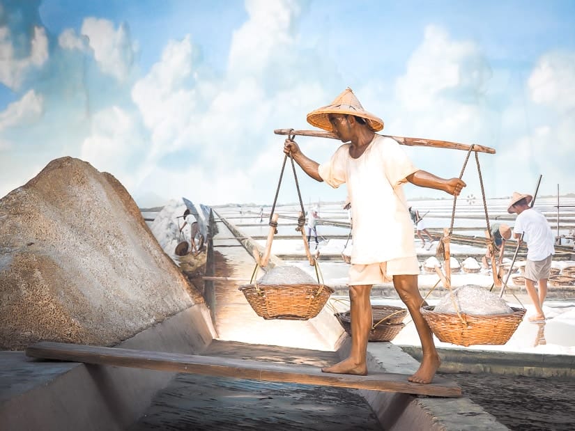 Display at Taiwan Salt Museum showing a man carrying baskets of salt in the salt fields