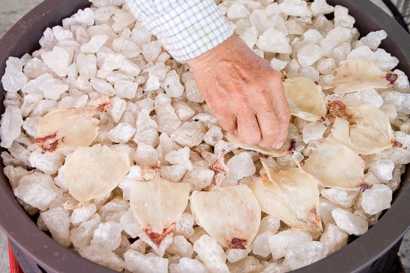 A hand grabbing some dried squid being roasted over salt chunks at Qigu Salt Mountain