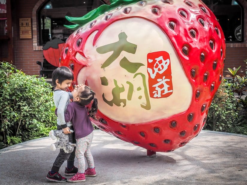 Two kids playing in front of a strawberry statue in Dahu, Taiwan