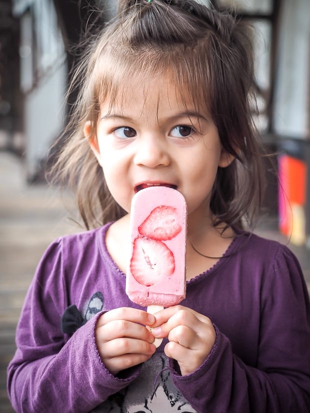 Young girl licking a strawberry popsicle