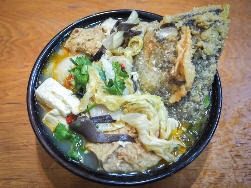 A bowl of Taiwanese stew with cabbage, tofu, mushrooms, and a whole fried fish head sticking out
