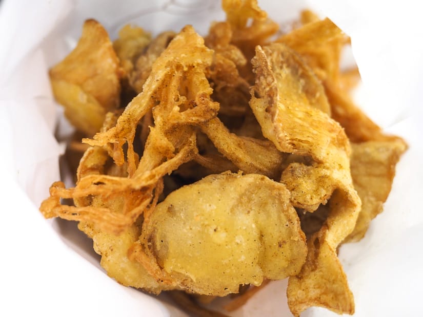 Looking into a white paper bag of various types of deep fried mushrooms