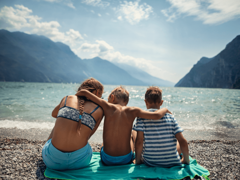 Kids sitting on a pebble beach at Lake Garda in the Italian lakes region