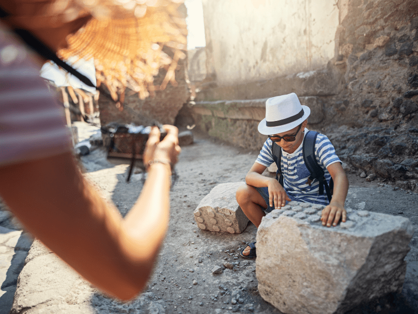 A parent taking a picture of a kid who is playing amongst the ruins of Pompeii