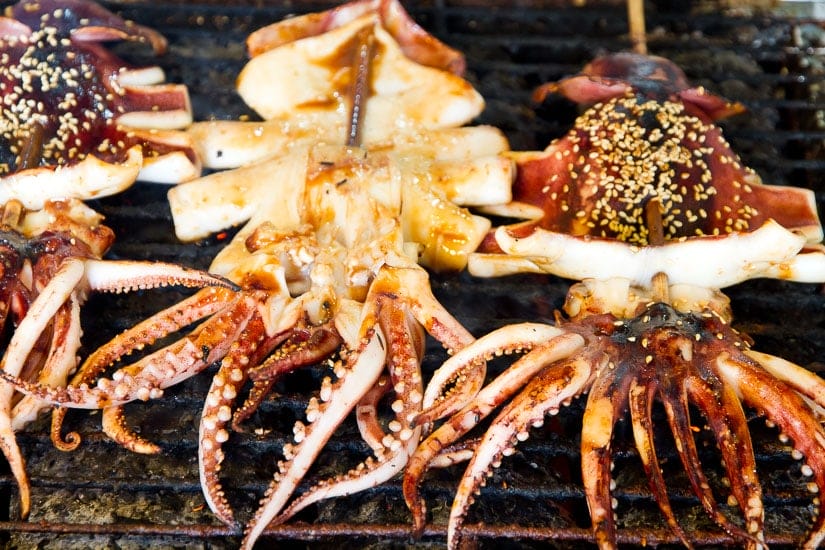 Three whole squids being grilled on a barbecue