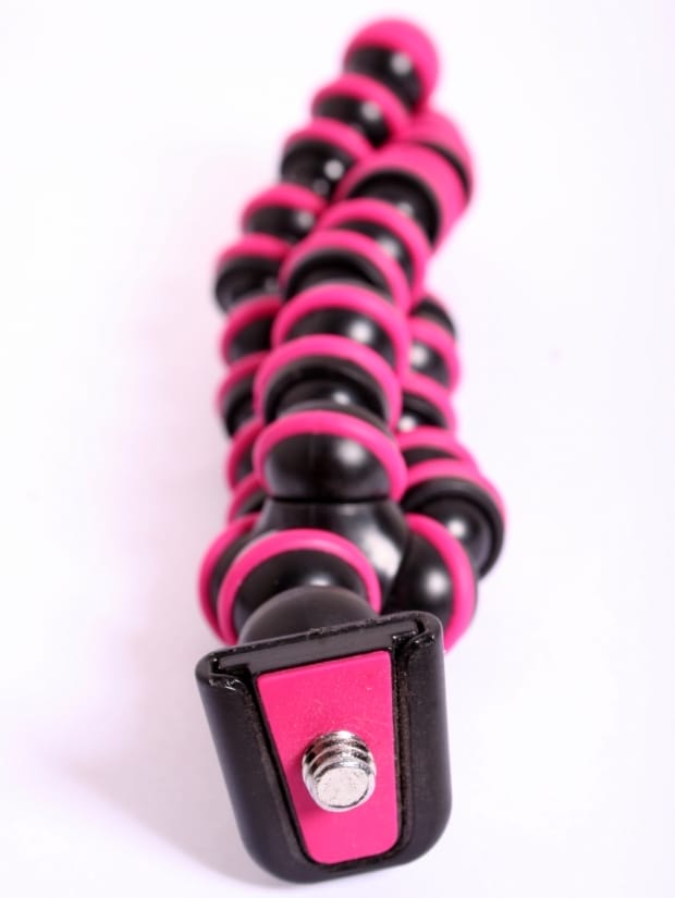 A pink and black camera tripod with the three legs intertwined, lying on a table, viewed from the the top head down