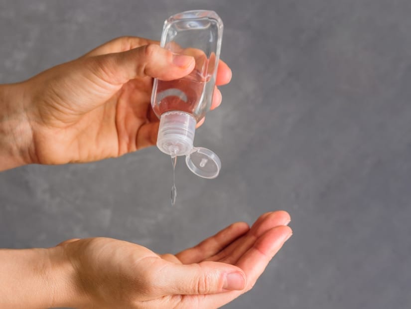 Close up of a hand pouring sanitizer from a small bottle into the person's other hand, which is cupped at the bottom, and a gray background