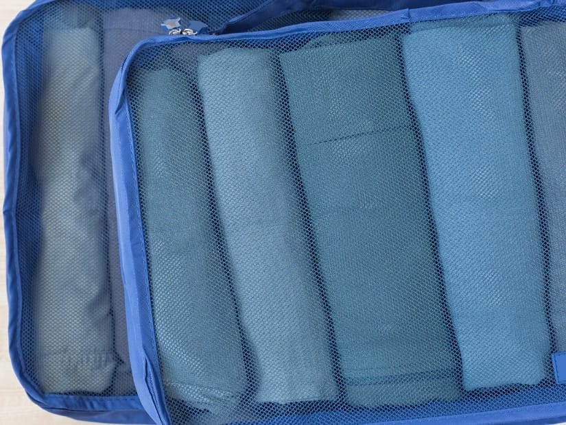 Two blue travel packing cubes viewed from above, each containing several rolled up blue shirts