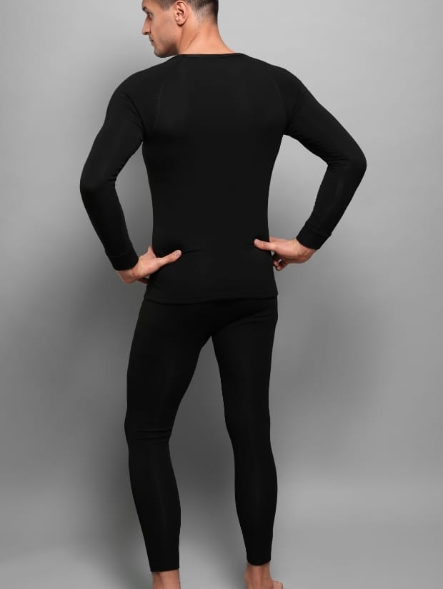 A man shot from behind, wearing tight black thermal underwear on top and bottom, with gray background
