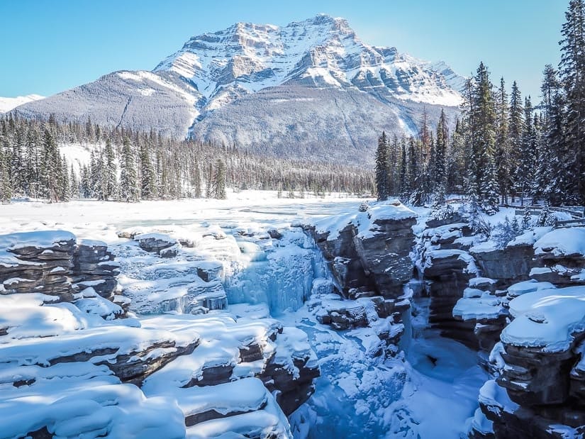 View of Athabasca Falls in winter backed by snowy mountains
