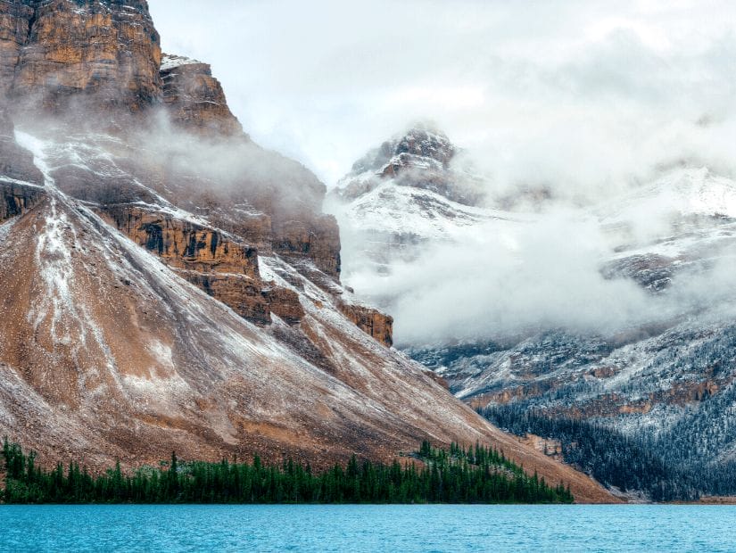 Aquamarine colored Bow Lake in Banff with cloud-covered mountains in background