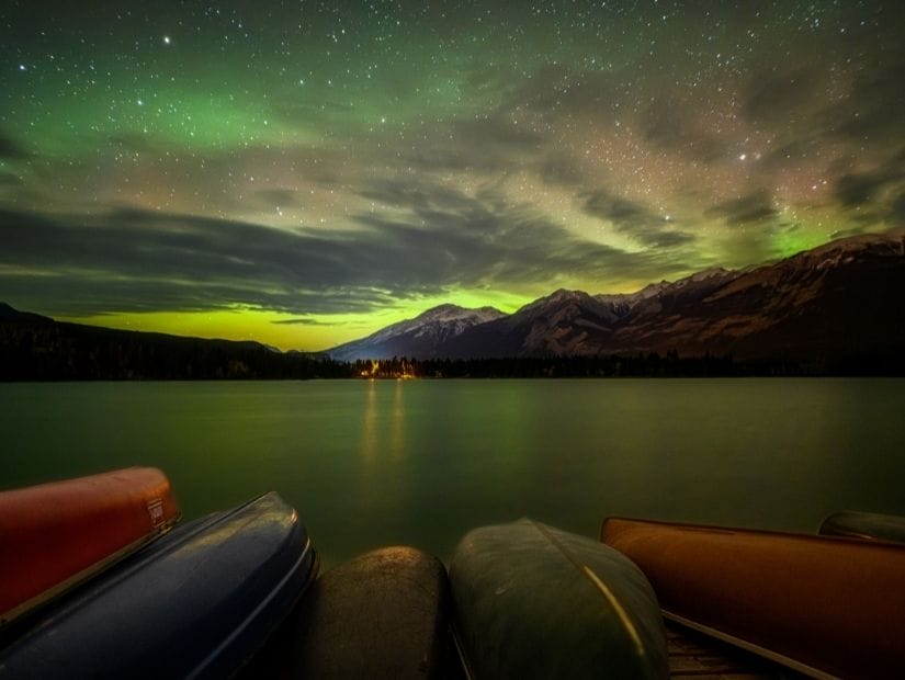 Canoes on the shore of Edith Lake in Jasper with Northern Lights in the sky
