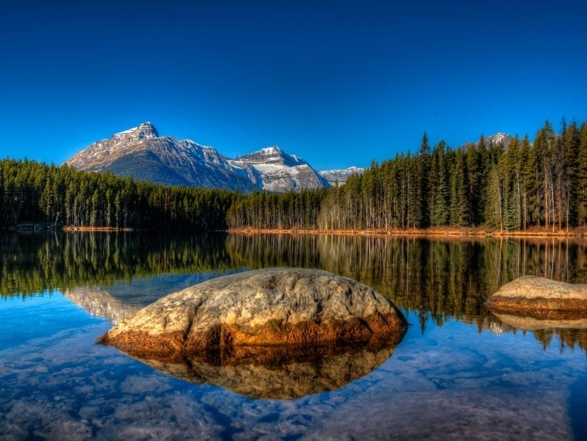 Large rock, trees, and mountain reflecting on the surface of Herbert Lake, one of the most beautiful lakes in Banff
