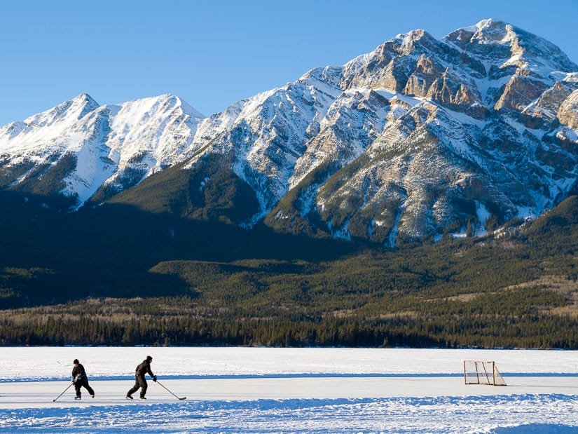 Two people playing hockey on Pyramid Lake in Jasper, with Pyramid Mountain in the background