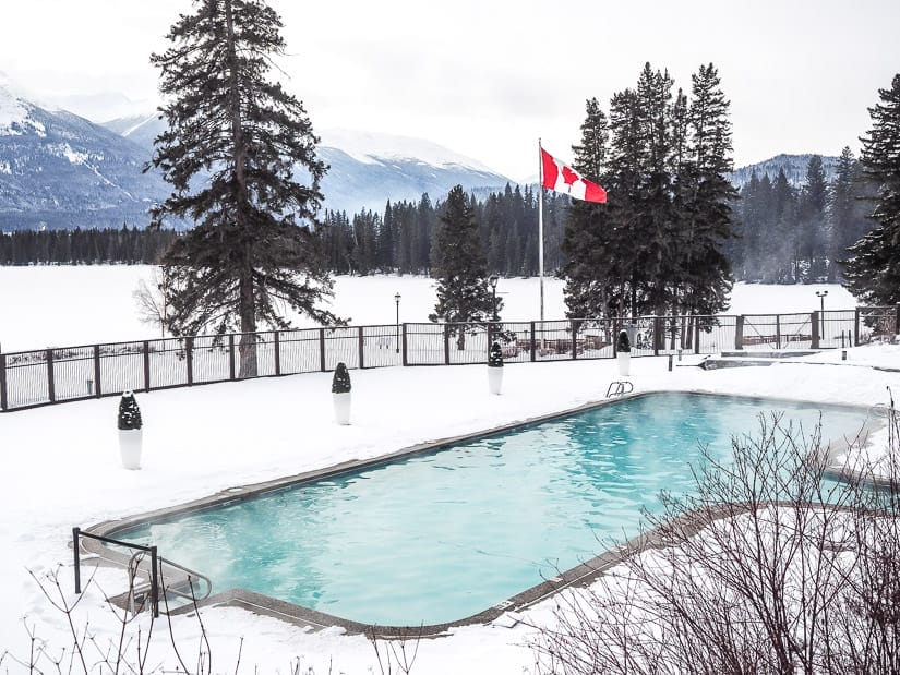 An outdoor pool surrounded by snow with Canadian flag on a pole