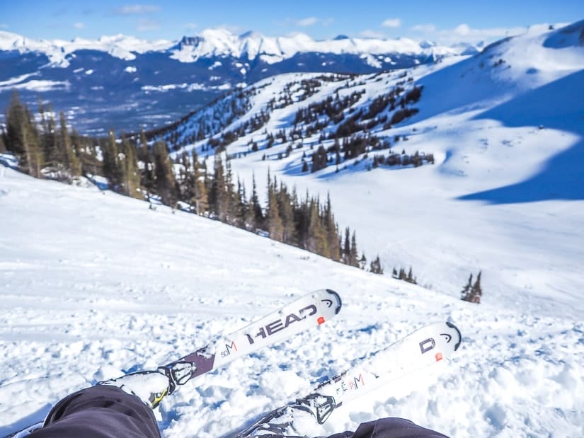 The tips of a pair of skis belonging to a person who is sitting on a ski hill at Marmot Basin Ski Resort, with a mountainous view in the distance