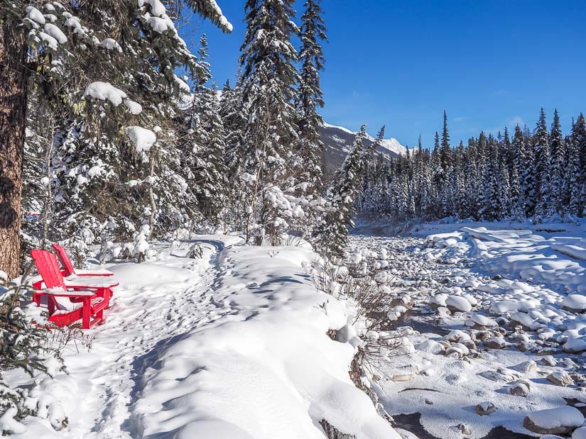 Two Parks Canada red chairs beside a snowy river at Lower Maligne Day Use Area in Jasper