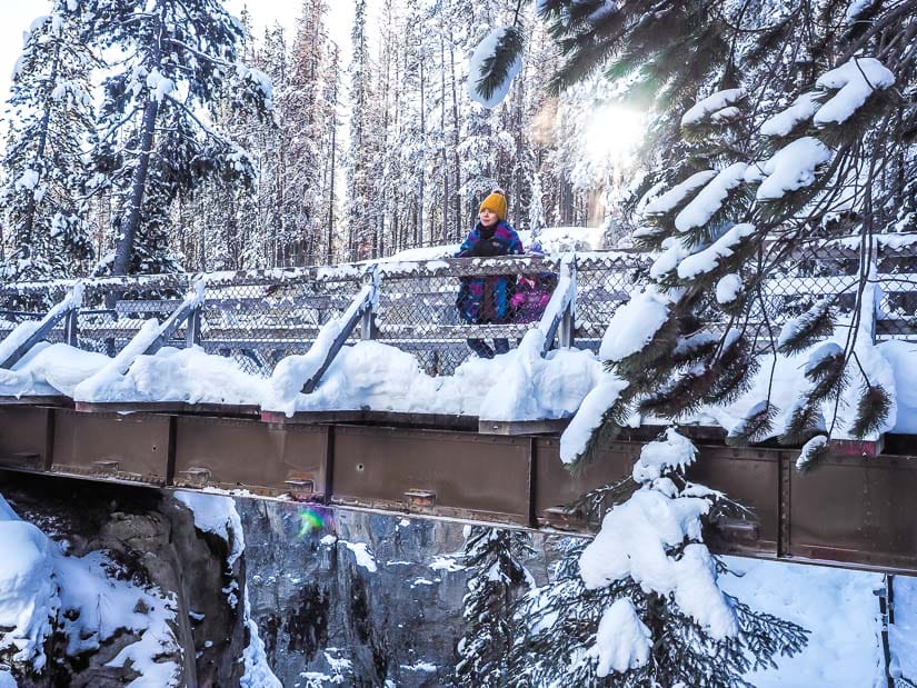Bridge across Sunwapta Falls in winter with a woman looking down at the waterfall