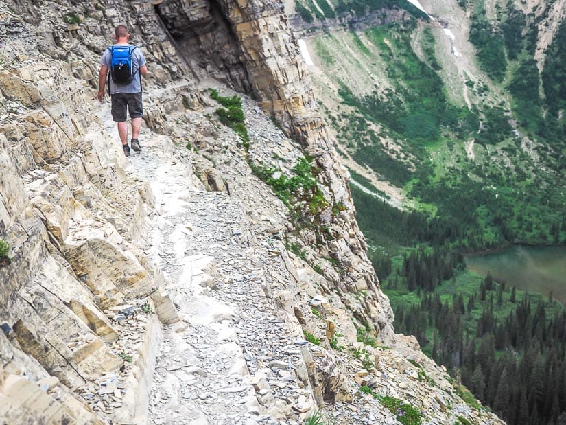Hiker walking on a narrow trail with a vertical cliff on the way to Crypt Lake 