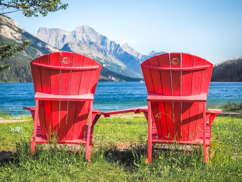 Two bright red Parks Canada chairs facing the lake and mountains in Waterton National Park