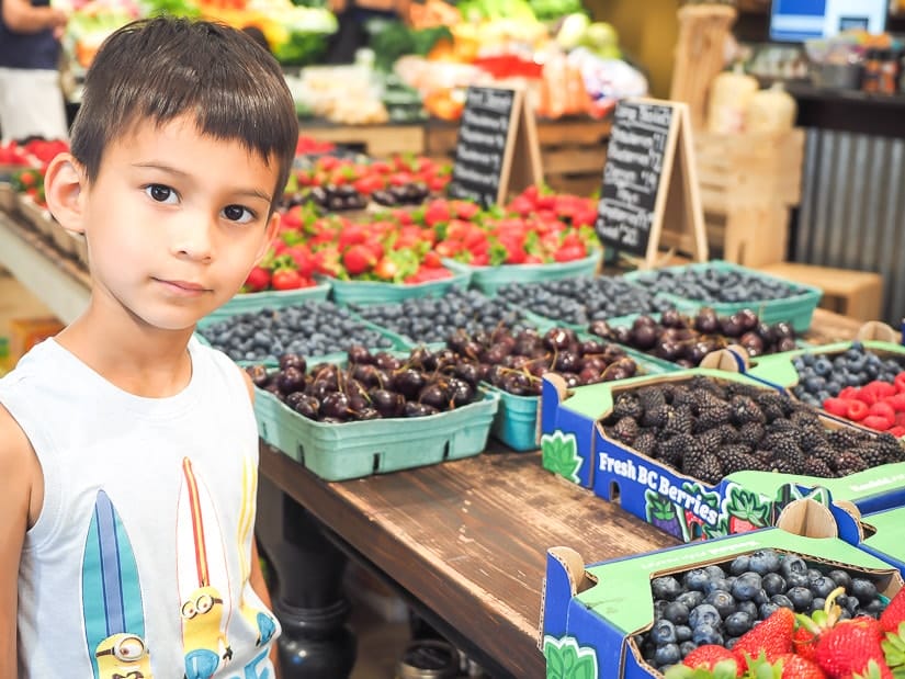 Kid standing in front of baskets of berries in a fruit market in Abbotsford