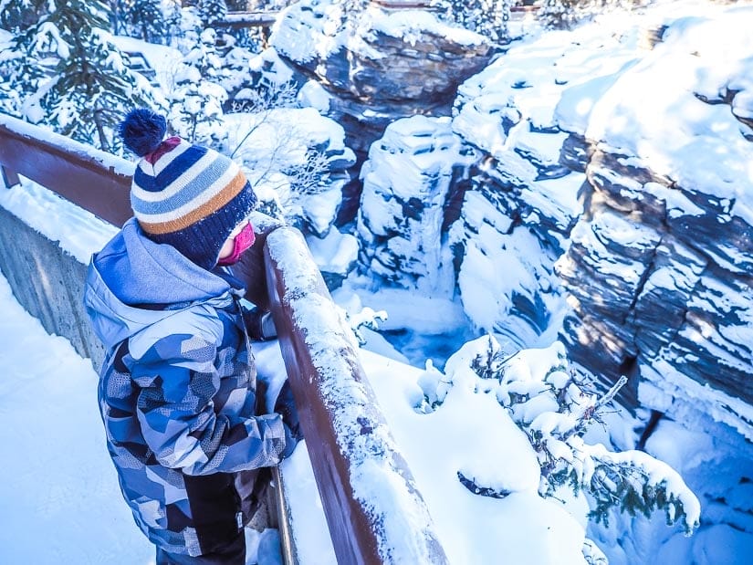 A kid looking over the railing at Athabasca Falls in winter