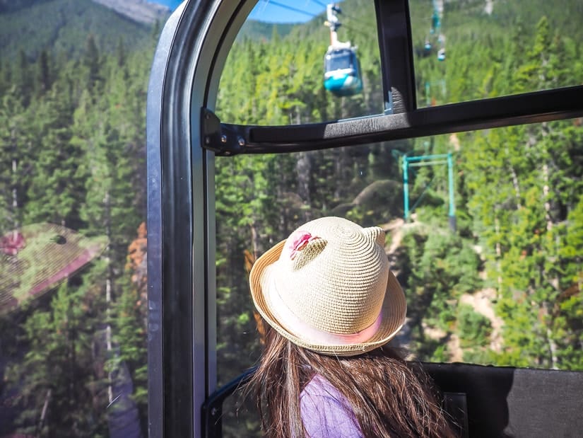 A girl sitting in Banff Gondola and looking up at other gondolas coming down the mountain