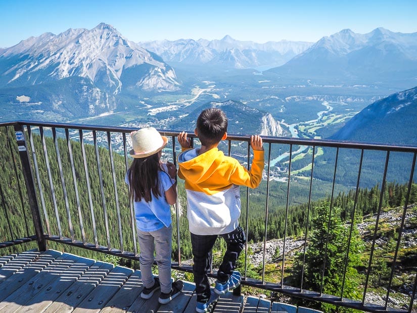 Two kids looking at the view of banff town from the peak of Sulphur Mountain