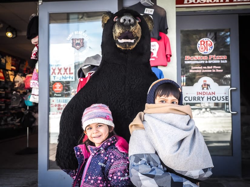 Two kids standing in front of a fake black bear in Banff town