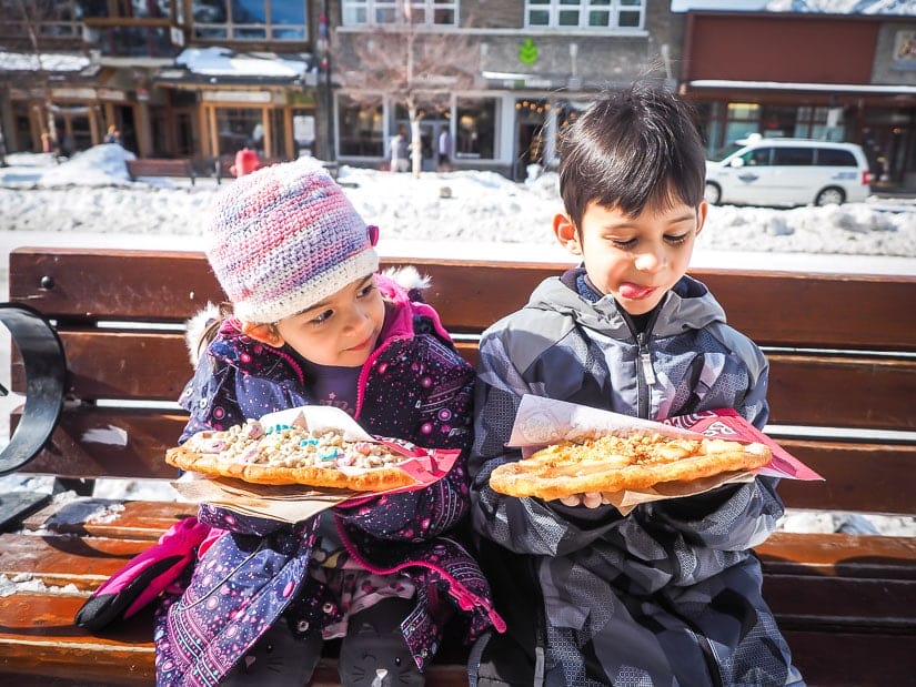 Two kids sitting on a bench on Banff Avenue about to eat Beaver Tails, one of the best treats for kids in Banff