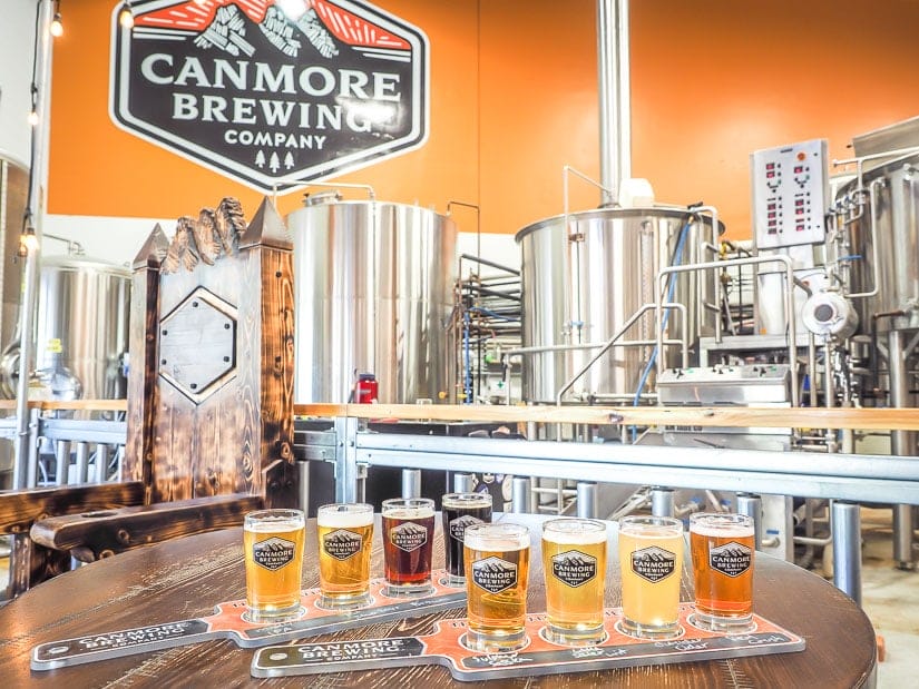 Two flights of beer samples on a table with brewing equipment behind at Canmore Brewing Company