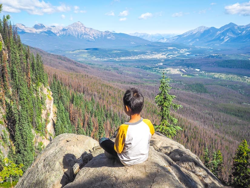 A boy sitting on a rock with a dramatic view of a valley in front of him at Edge of the World in Jasper