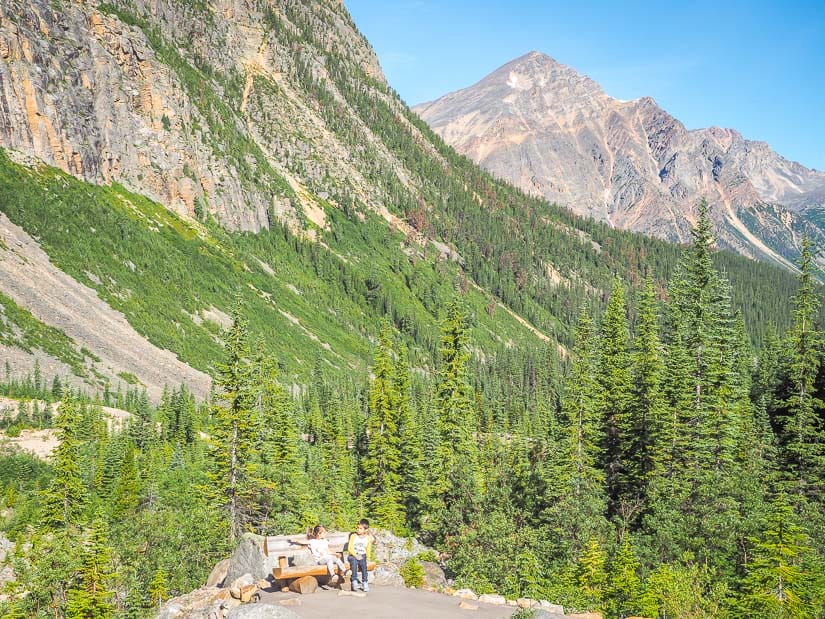 Two kids sitting on a bench on Edith Cavell Meadows Trail with mountains in the background