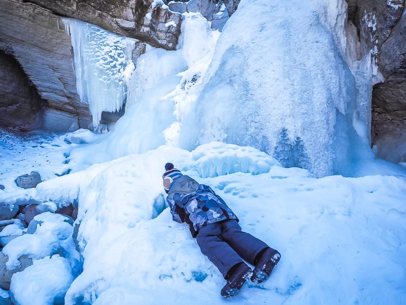 A kid lying on the ice and looking down a crack.