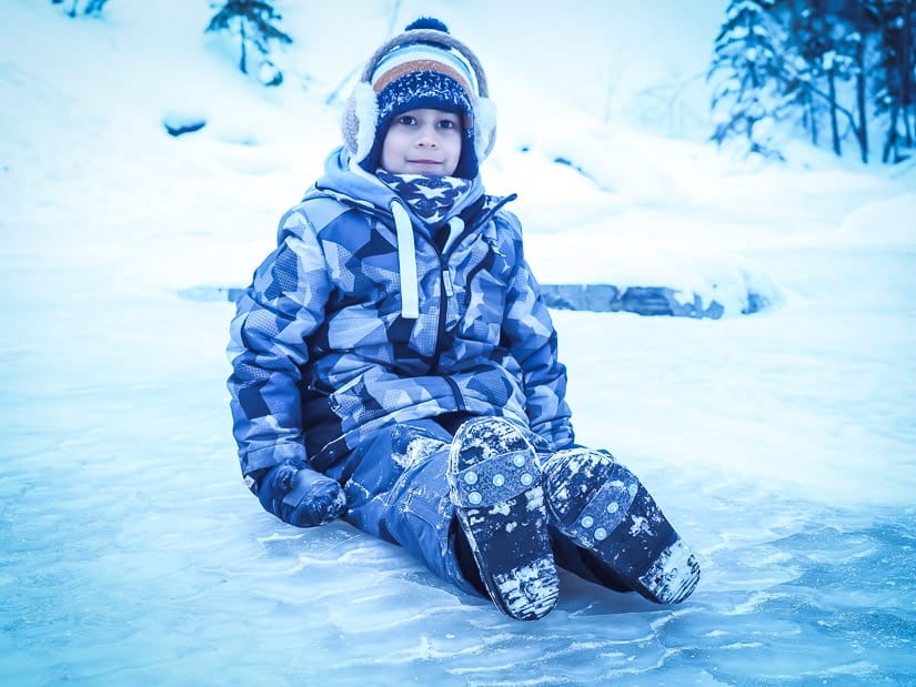 A kid sitting on the ice and wearing ice cleats on his shoes for the Maligne Canyon Icewalk
