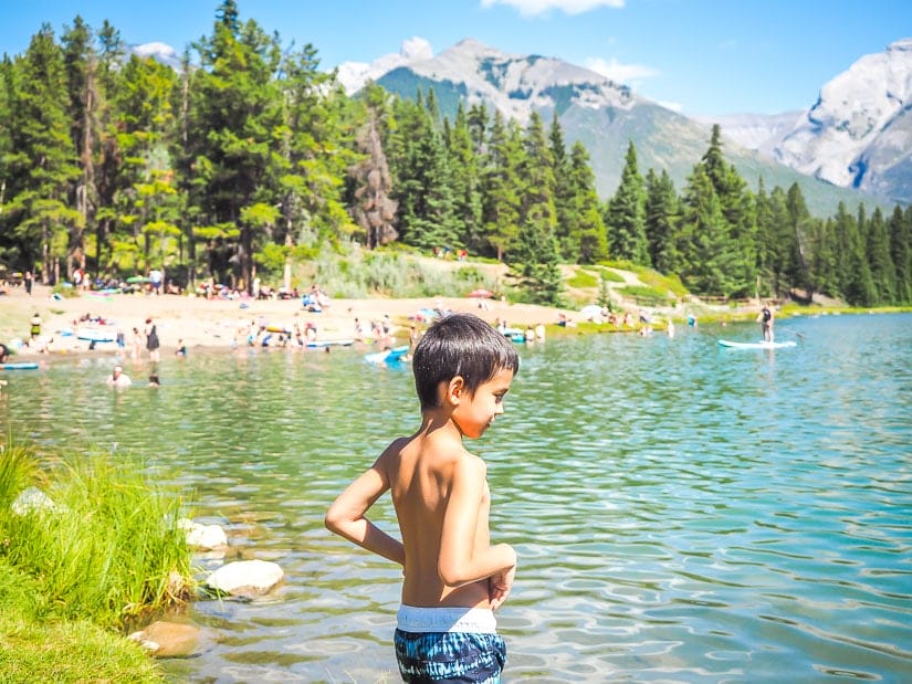 A kid standing by the beach at Johnson Lake, one of the best swimming spots in Banff