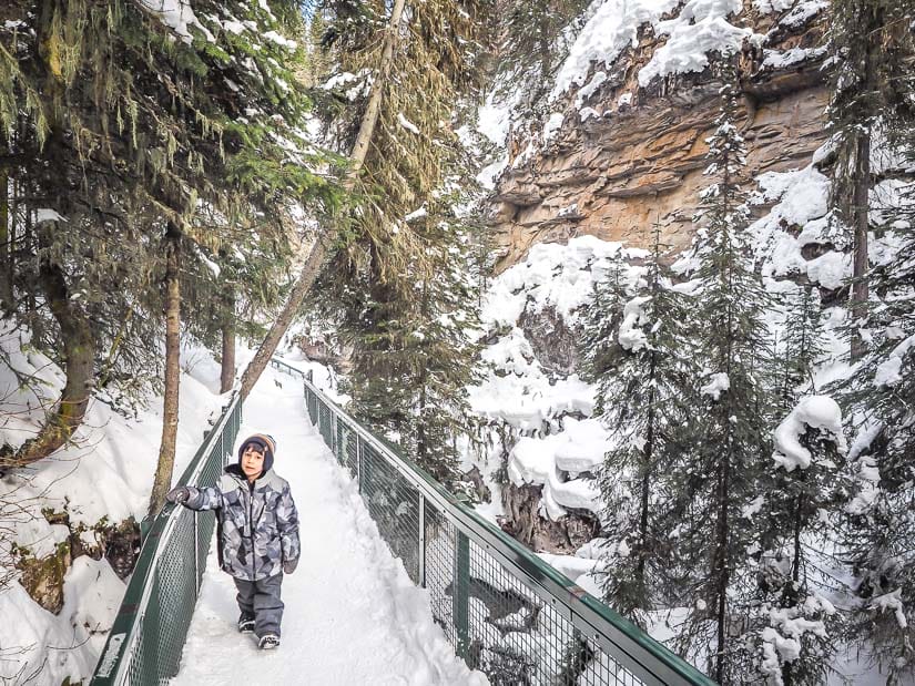 A kid walking on a snow-covered trail in Johnston Canyon