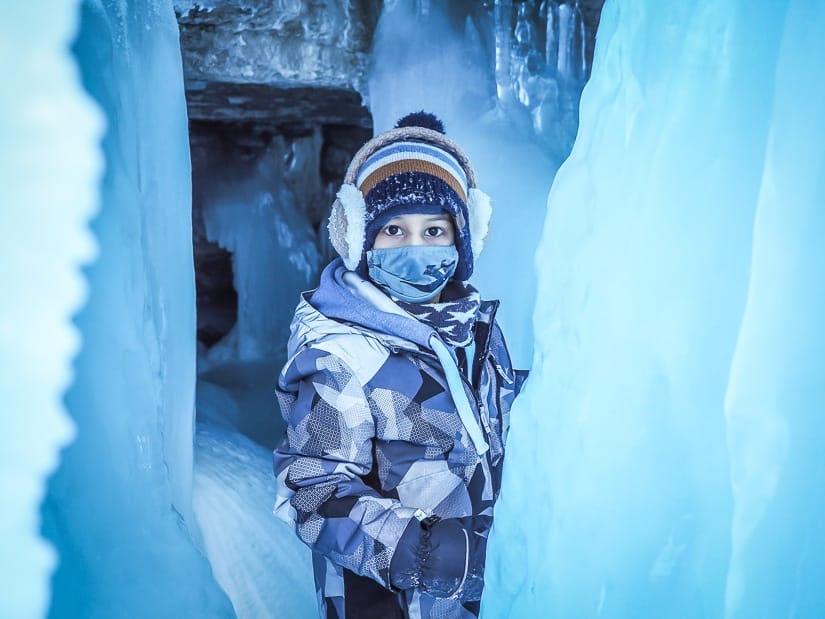 A kid standing behind a frozen waterfall