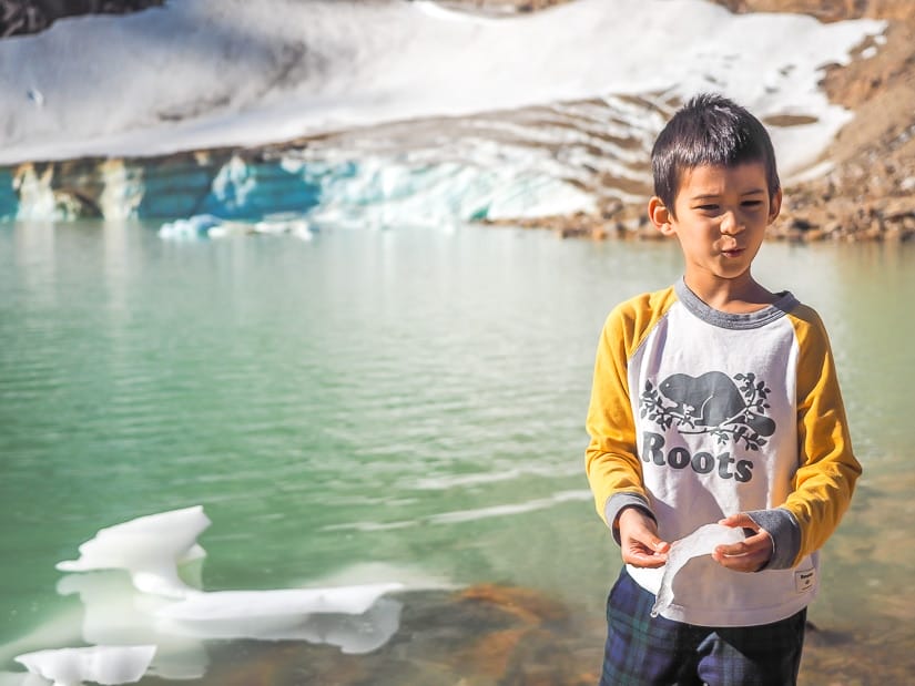 A boy standing by Cavell Pond holding a chunk of ice.