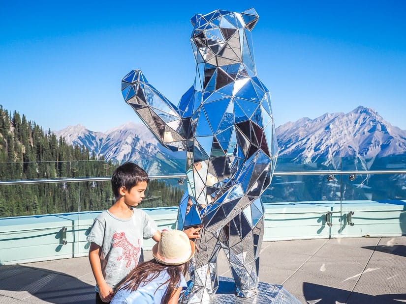 Two kids looking at a bear covered with mirrors on the rooftop observatory and Banff Gondola Upper Station
