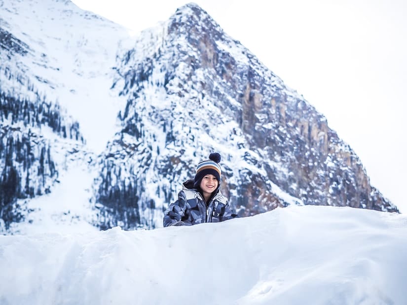 A kid climbing a snowy hill beside lake Louise with a mountain in the background.